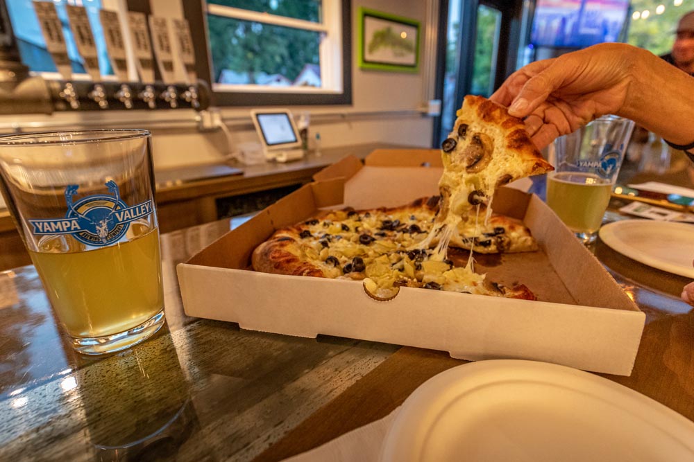 Patron pulling a slice of Pizza out of a to go box from Embers.